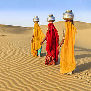 Indian women crossing sand dunes and carrying on their heads water from local well, Thar Desert, Rajasthan, India. Rajasthani women and children often walk long distances through the desert to bring back jugs of water that they carry on their heads. 