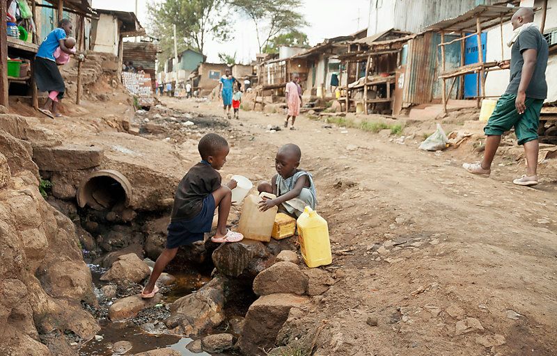Two little boys in the street are pouring water form the river in cans, in Nairobi, Kenya.