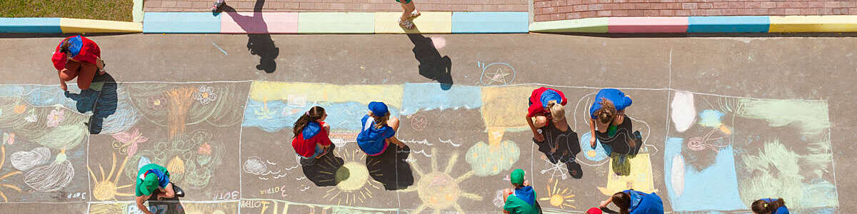  Overhead view of kids coloring a picture with colored chalk in driveway.  