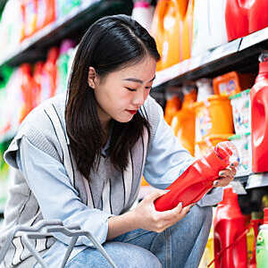Close-up of woman holding a red bottle of washing detergent beside a well-stocked supermarket shelf.