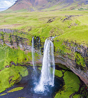 Plunging view of a waterfall jutting out of craggy green cliffs.