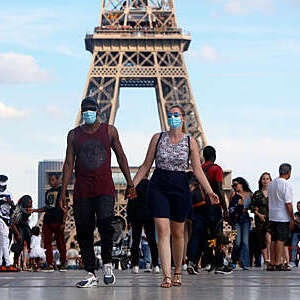 Couple wearing a protective mask walk a front the Eiffel Tower in France.