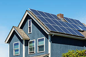 Small-town American home with blue slatted wall cladding and solar panels on the roof.