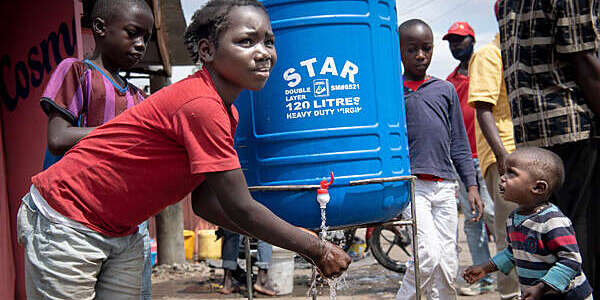 Children of varying ages in brightly coloured T-shirts wash their hands at a hand-washing station in a Nairobi slum.