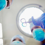 An assistant passing a surgical scissors to the surgeon, in an operating room.